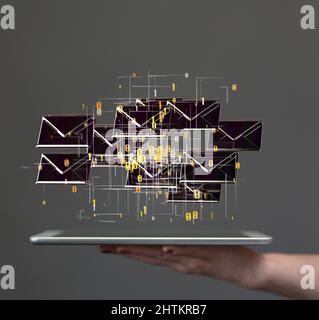 Collection of illustrative email symbols surrounded with binary code floating on top of a tablet Stock Photo
