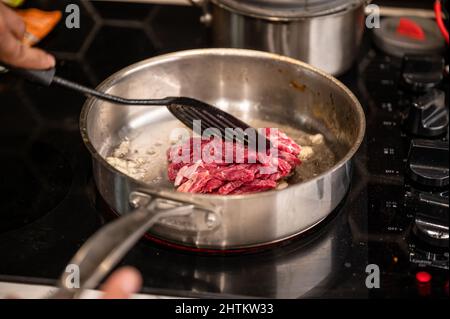 Hand using kitchen flipper frying sliced beef in iron pan on electric stove Stock Photo