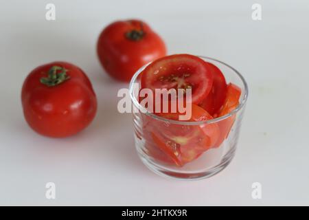 Slices of tomato in a glass bowl, shot on a white background along with fresh tomatoes. Stock Photo