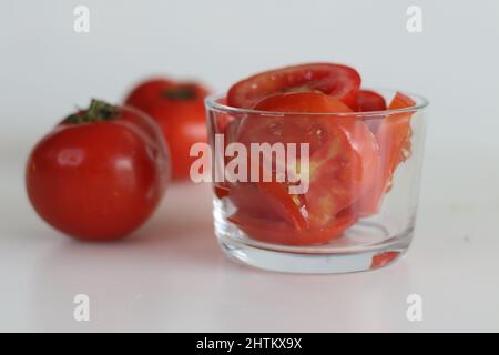 Slices of tomato in a glass bowl, shot on a white background along with fresh tomatoes. Stock Photo