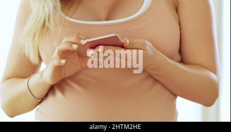 Staying in touch with everyone before the big day. Cropped shot of an unrecognizable pregnant woman using a cellphone at home. Stock Photo