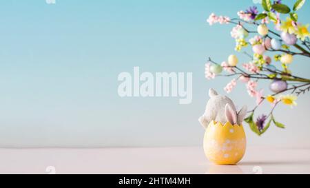 A white rabbit hid in an Easter egg on a blue background. Festive Easter card. Copy space.  Stock Photo