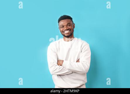 A young African-American man in a white T-shirt laughs on a blue isolated background Stock Photo