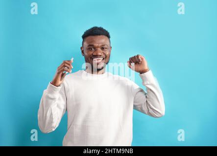 Portrait of an attractive cheerful dark-skinned man using a device to communicate in his spare time, isolated on a bright blue background Stock Photo