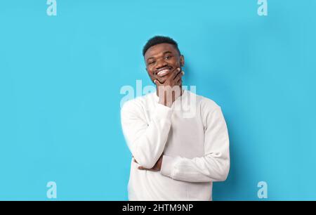 A young African-American man in a white T-shirt laughs on a blue isolated background Stock Photo