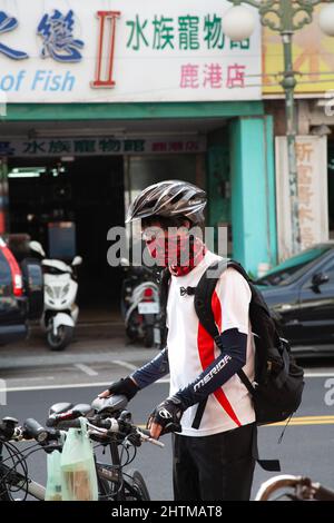 A cyclist wearing a gaiter facemask and helmet in the street in Lukang Township, Changhua County, Taiwan Stock Photo