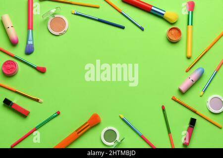 Frame made of makeup brushes and cosmetic products on green background Stock Photo