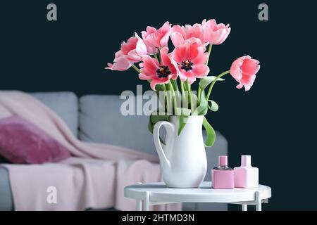 Vase with tulips and bottles of perfume on table in dark living room