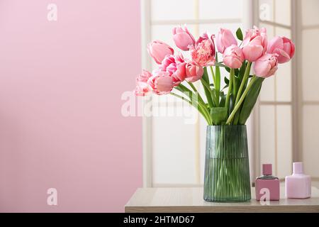 Vase with pink tulips and bottles of perfume on table in room