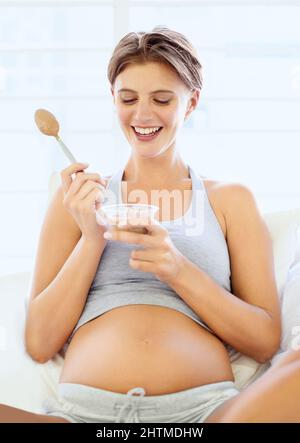 Mommy needs some sugar. A happy young pregnant woman eating a small bowl of pudding. Stock Photo