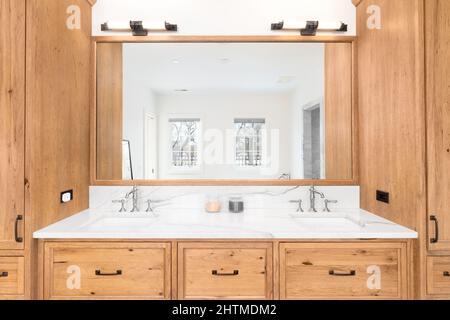 A large, wooden vanity cabinet in a luxury bathroom with marble countertops and two sinks. Stock Photo