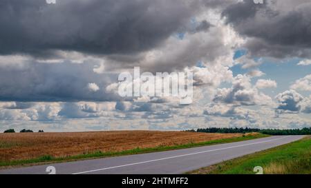 The rural road goes over the horizon. Storm clouds over the field. Stock Photo