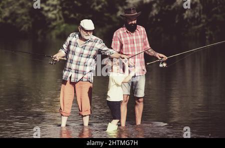 Family generation and people concept. Father teaching son how to fly-fish in river. Man in different ages. Stock Photo