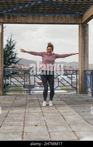 young beautiful brown haired caucasian woman jumping on the street looking at camera smiling Stock Photo