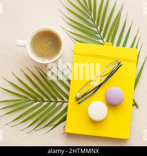 office table with yellow notepad, cup of coffee, glasses, macaroons on palm Stock Photo