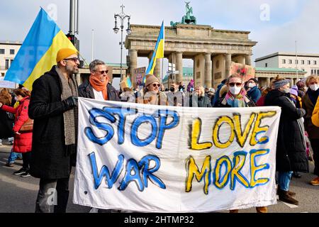 People with placards participate in a protest against the war in Ukraine near Brandenburg Gate. Text Stop War Love More on textile. Stock Photo