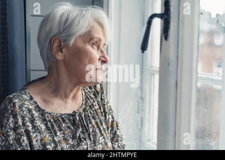 grey-haired caucasian pensioner lady looking sadly out of the window medium close up indoor shot. High quality photo Stock Photo