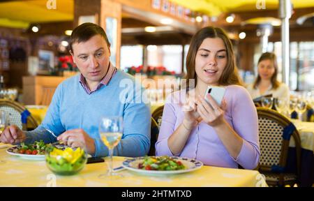Woman using smartphone in restaurant during dinner with her husband Stock Photo