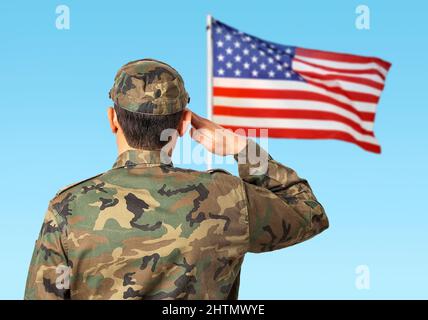 Rear view of a young soldier standing to a the US flag and saluting Stock Photo