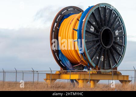 Bulk sub-sea industrial glass fiber optic cable on a metal spool on a ship's stand. The orange data line is coiled around a black reel in storage. Stock Photo