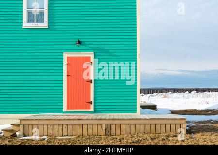 An exterior single traditional wooden shutter door with cream color trim on a teal green color wall of a house with a single hung window. Stock Photo