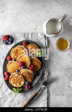 Pancakes in ceramic plate with berries, mint leaves, gravy boats and fork on napkin, top view Stock Photo