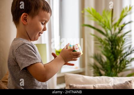 Cute baby boy assembling multicolored Rubik's cube solving logical game lying on couch at home Stock Photo