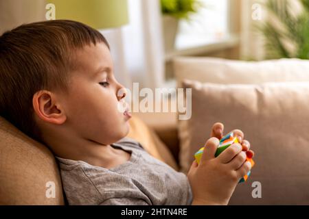 Cute baby boy assembling multicolored Rubik's cube solving logical game lying on couch at home Stock Photo