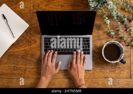 Overhead view of hands of woman typing on laptop on old wooden desk Stock Photo