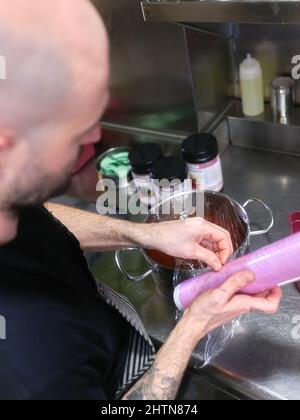 Cook wrapping a pot of sauce with cling wrap Stock Photo
