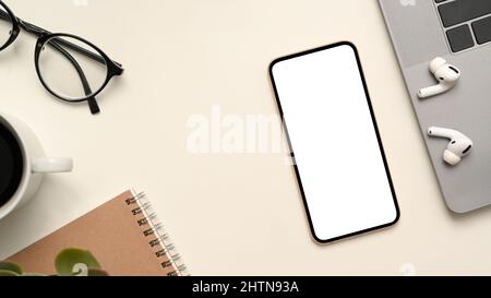 Modern workspace table with laptop computer, earbuds, glasses, coffee cup, notebook and smartphone white screen mockup on white background. top view Stock Photo