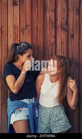 When I say I wont tell anyone my best friend doesnt count... Two young friends standing outdoors sharing secrets. Stock Photo