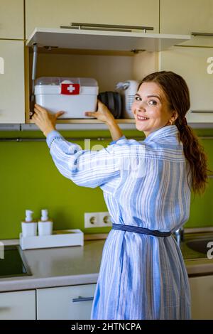 Domestic woman putting first aid kit with vitamins, drugs, antibiotics and cure at kitchen cupboard Stock Photo