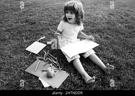 Kids Exam Study. Funny little student boy reading book outdoors, lying on lawn in park, studying at School backyard. Stock Photo