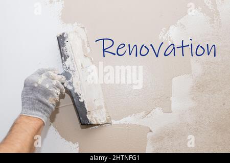 Renovation text on wall.Man plastering wall with putty-knife, preparation for painting.Hands of worker with wall plastering tools. Plasterer Stock Photo