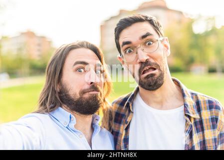 funny gay couple looking at camera making grimaces in park. Stock Photo
