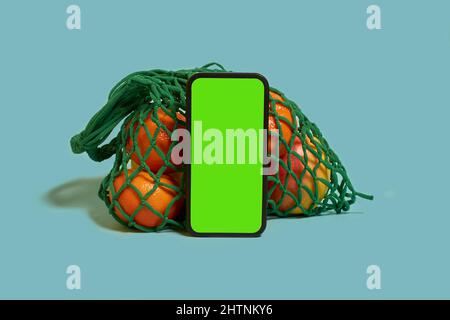 A smartphone with a green screen, fruits and citrus in a mesh bag  Stock Photo