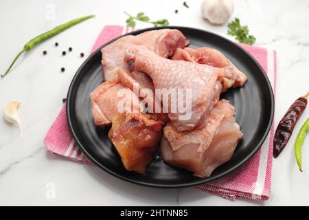 Clean and Raw Chicken on a black plate with Indian spices and cooking ingredients. Along with copy space. Chicken curry cut. Biryani cut chicken Stock Photo