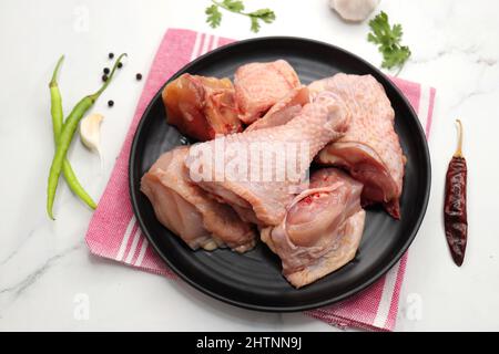 Clean and Raw Chicken on a black plate with Indian spices and cooking ingredients. Along with copy space. Chicken curry cut. Biryani cut chicken Stock Photo