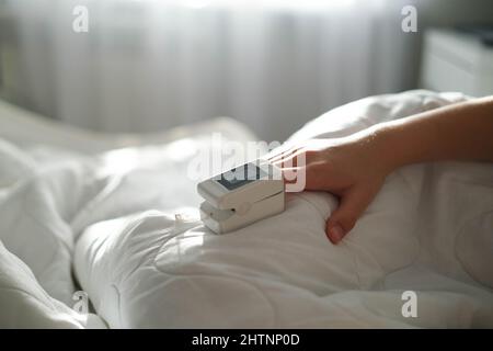 The teenager lies in bed and measure the oxygen saturation with a pulse oximeter. Asthma treatment. The sick child lies in bed. Bedroom or hospital ro Stock Photo