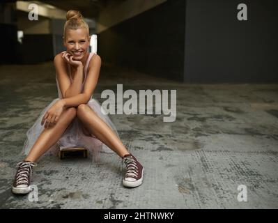 Swapping slippers for sneakers. A beautiful ballerina sitting on a skateboard wearing sneakers. Stock Photo