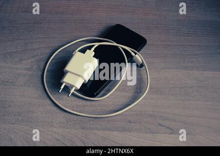 Charger with USB type C cable and smartphone on grunge style wooden table Stock Photo