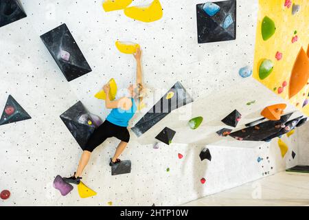 Woman climbing tall, indoor, man-made rock climbing wall Stock Photo