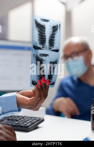 Closeup of therapist doctor hand holding lung radiography discussing medical expertise with invalid senior man during disease examination in hospital office. Concept of medicine during coronavirus Stock Photo