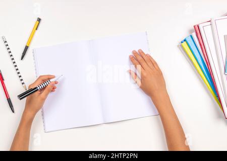 Kid hand holding pen in left hand and writing in open notebook, doing homework. Left Handers Day Stock Photo