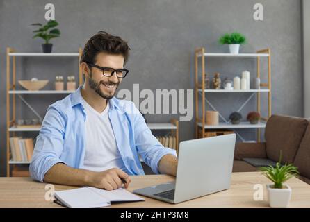 Happy Caucasian adult male student studying independently at home online using laptop. Stock Photo