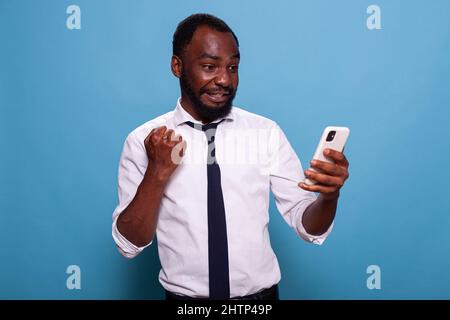 Man in white shirt holding smartphone winning online mobile game looking tensed at screen. Gamer testing mobile app on smart phone for the first time feeling enthusiastic. Stock Photo