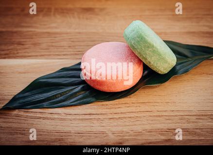 Pink and green color solid shampoo bars or conditioner bar on green leaf on wooden background. Minimalist beauty set indoors, copy space. Stock Photo
