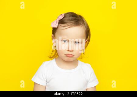 Little girl with sad expression on yellow background. children's emotions. Stock Photo