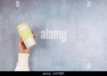 Sustainable living, zero waste, no plastic concept. Female hand holding stylish reusable eco friendly coffee cup on gray background Stock Photo